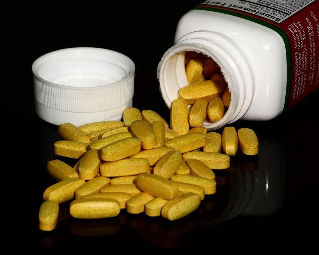 Vitamin bottles and a pile of round supplement tablets on a table.
