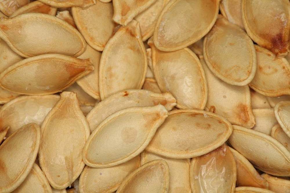 Green pumpkin seeds spread across a wooden board.